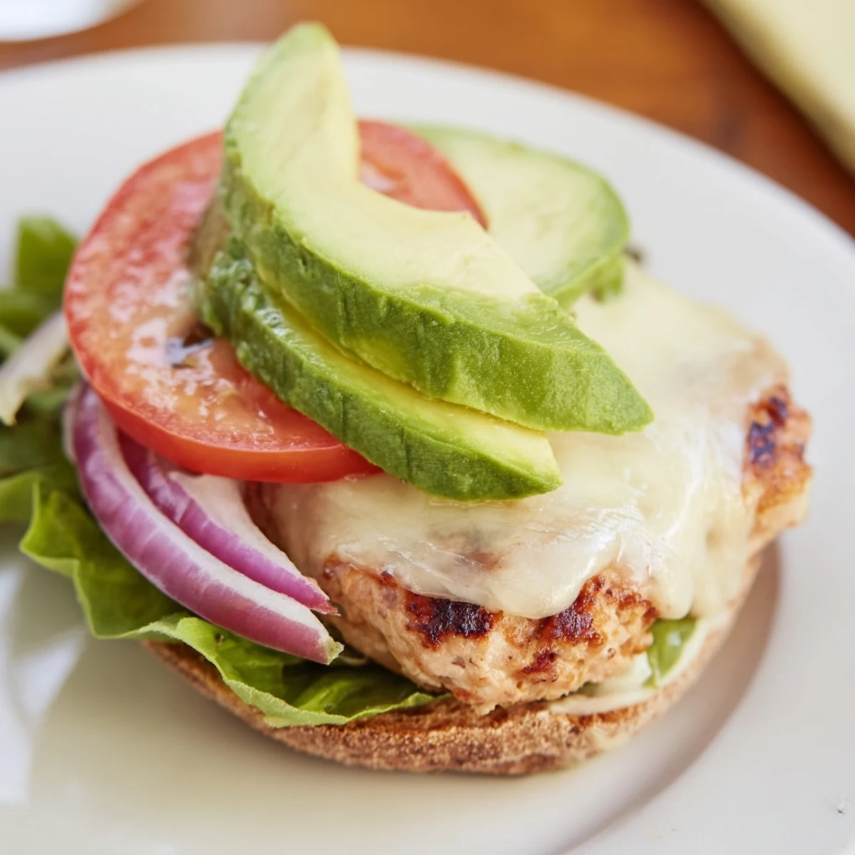 Perfectly cooked turkey burger patty topped with avocado, Swiss cheese, and lettuce on a whole wheat bun.