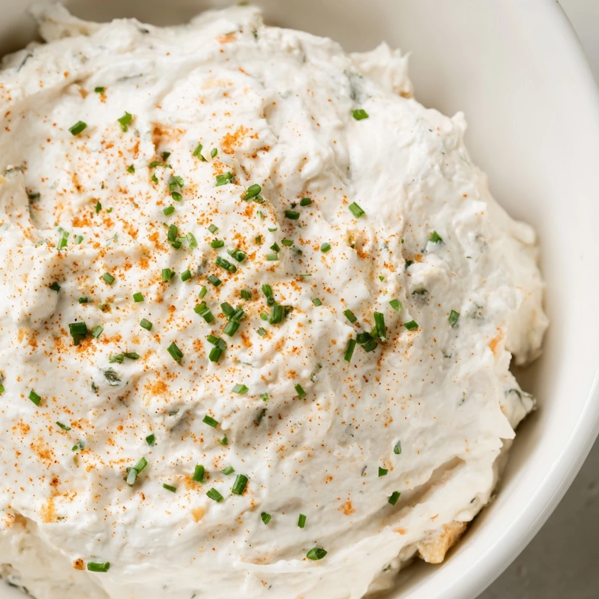 A bowl of creamy dip garnished with fresh chives and paprika, served with crisp carrot sticks and celery for dipping.