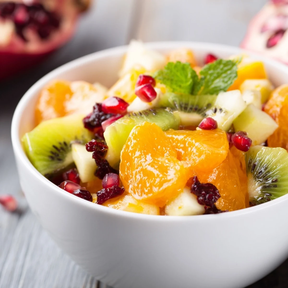 Bright Winter Fruit Salad with Honey Lime Dressing in a white bowl, topped with fresh mint leaves and vibrant pomegranate arils.