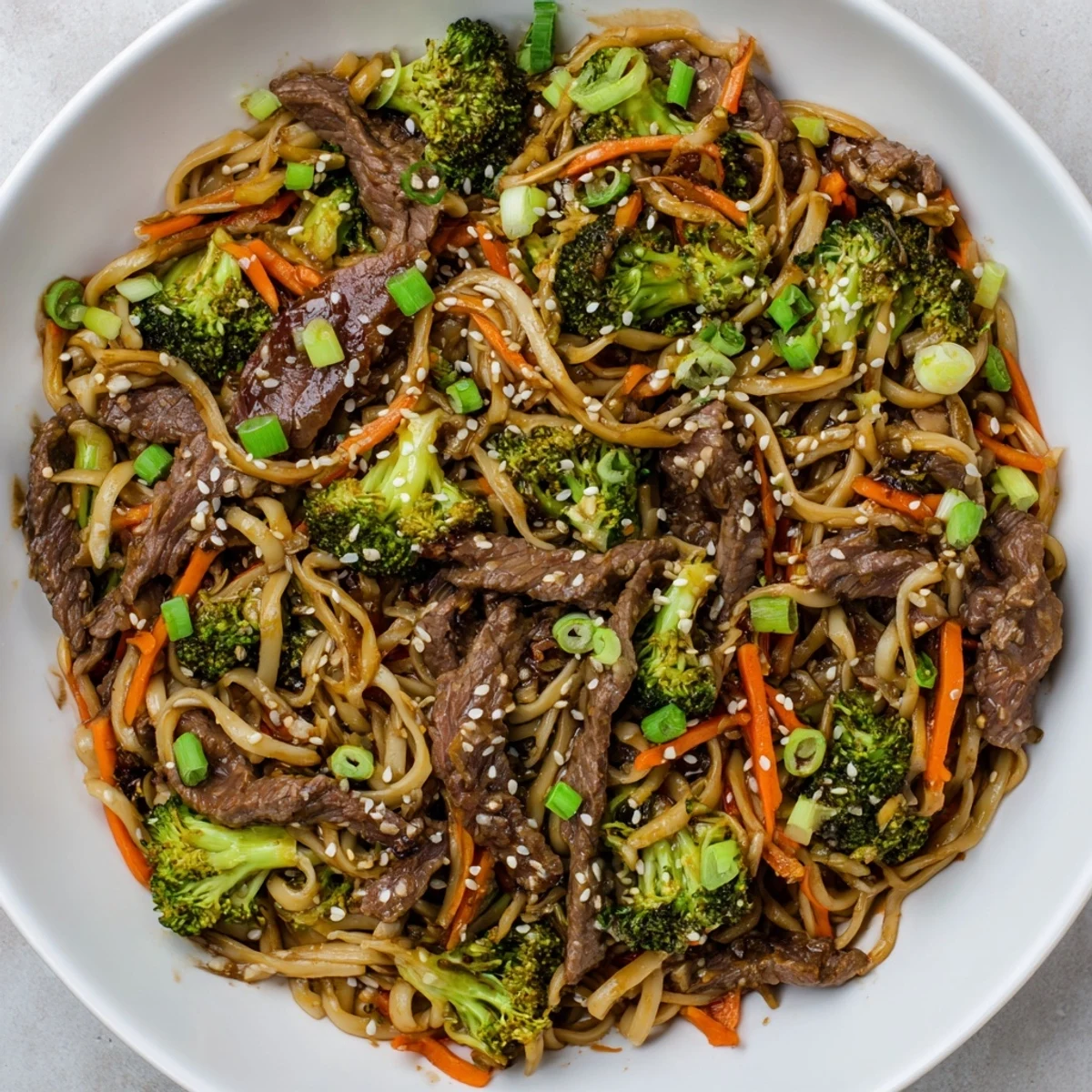 Steaming platter of Beef and Broccoli Lo Mein garnished with green onions and sesame seeds, served on a white plate.