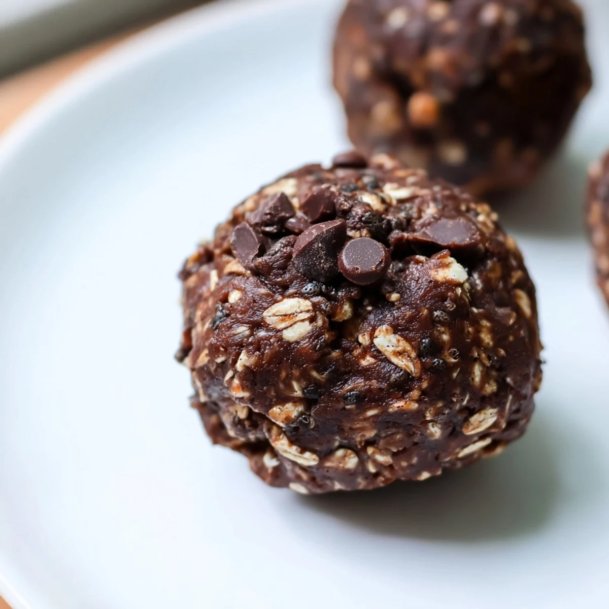 Chocolate Peanut Butter Energy Bites are stacked on a parchment-lined tray, with oats, cocoa powder, and mini chocolate chips scattered around the prep area.  