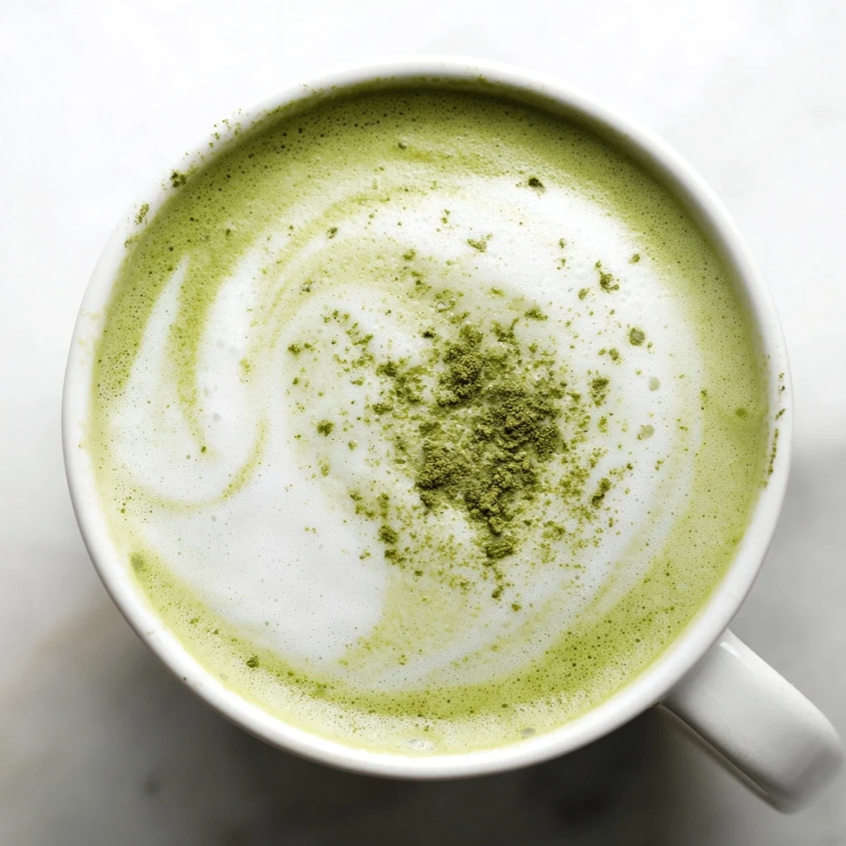 Close-up of a creamy Green Matcha Latte with almond milk, dusted with matcha powder beside a sweet pastry.