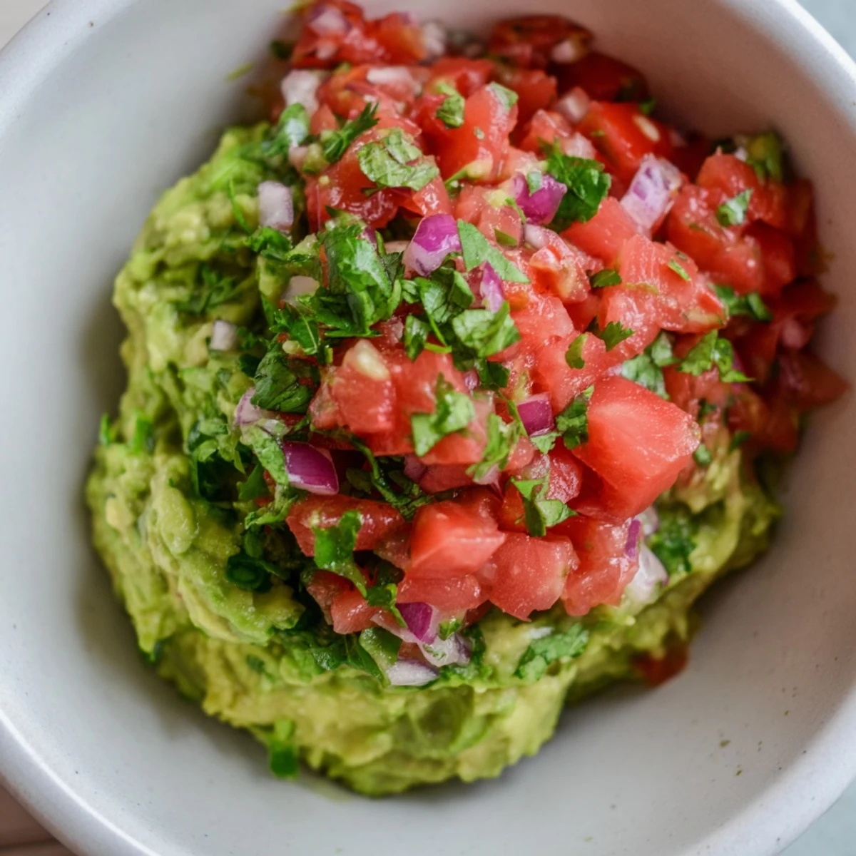 A vibrant bowl of Game Day Guacamole with Salsa, surrounded by crispy tortilla chips and fresh lime wedges for dipping.