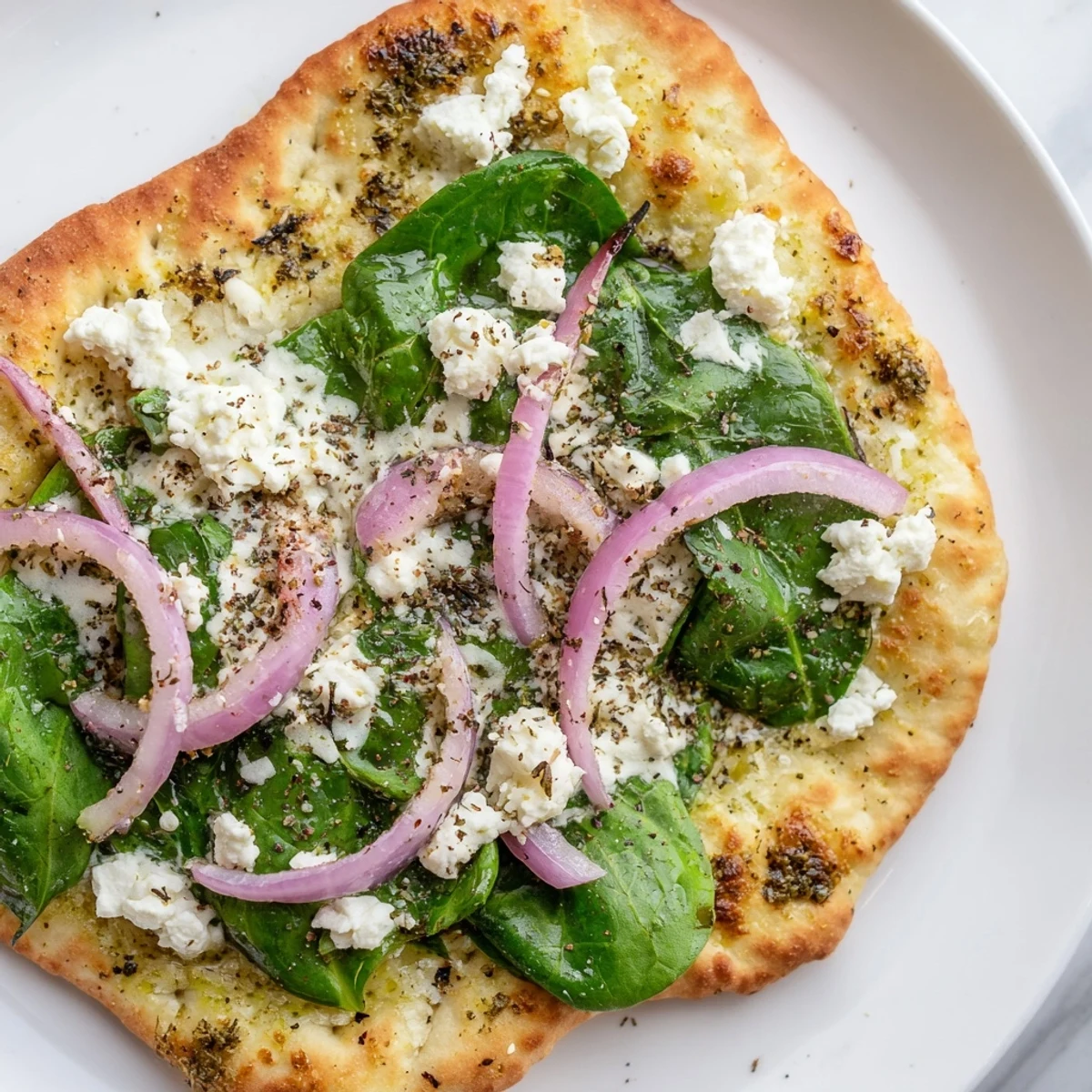 Mediterranean Spinach and Feta Flatbread Pizza on a plate, garnished with red onion and oregano, ready to serve.