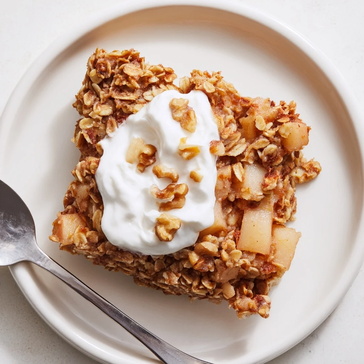 A cozy slice of Baked Apple Oatmeal with Greek Yogurt and toasted walnuts on plate.