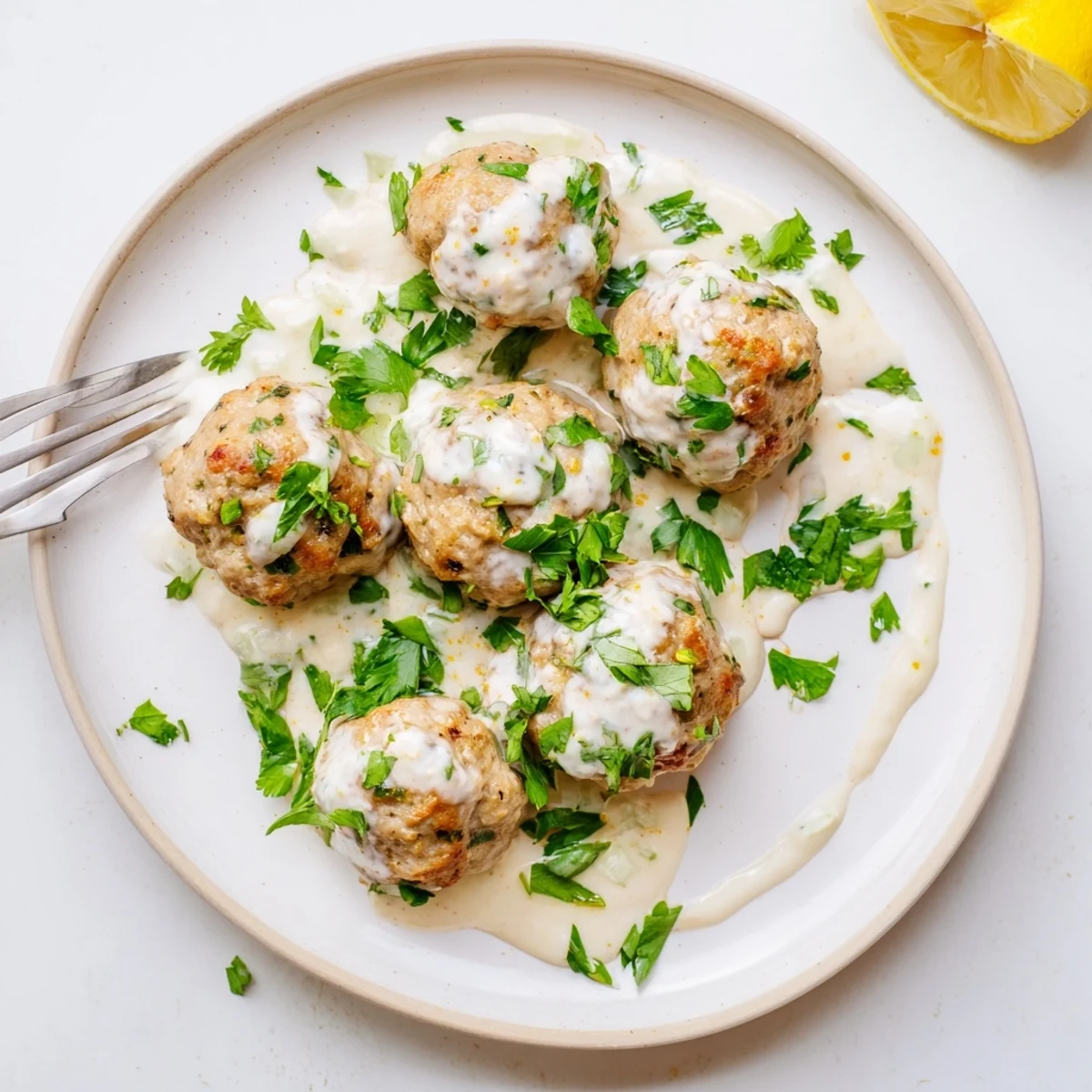 Close-up of Chicken Kofta resting on a platter with lemon wedges and a rich yogurt dip.  