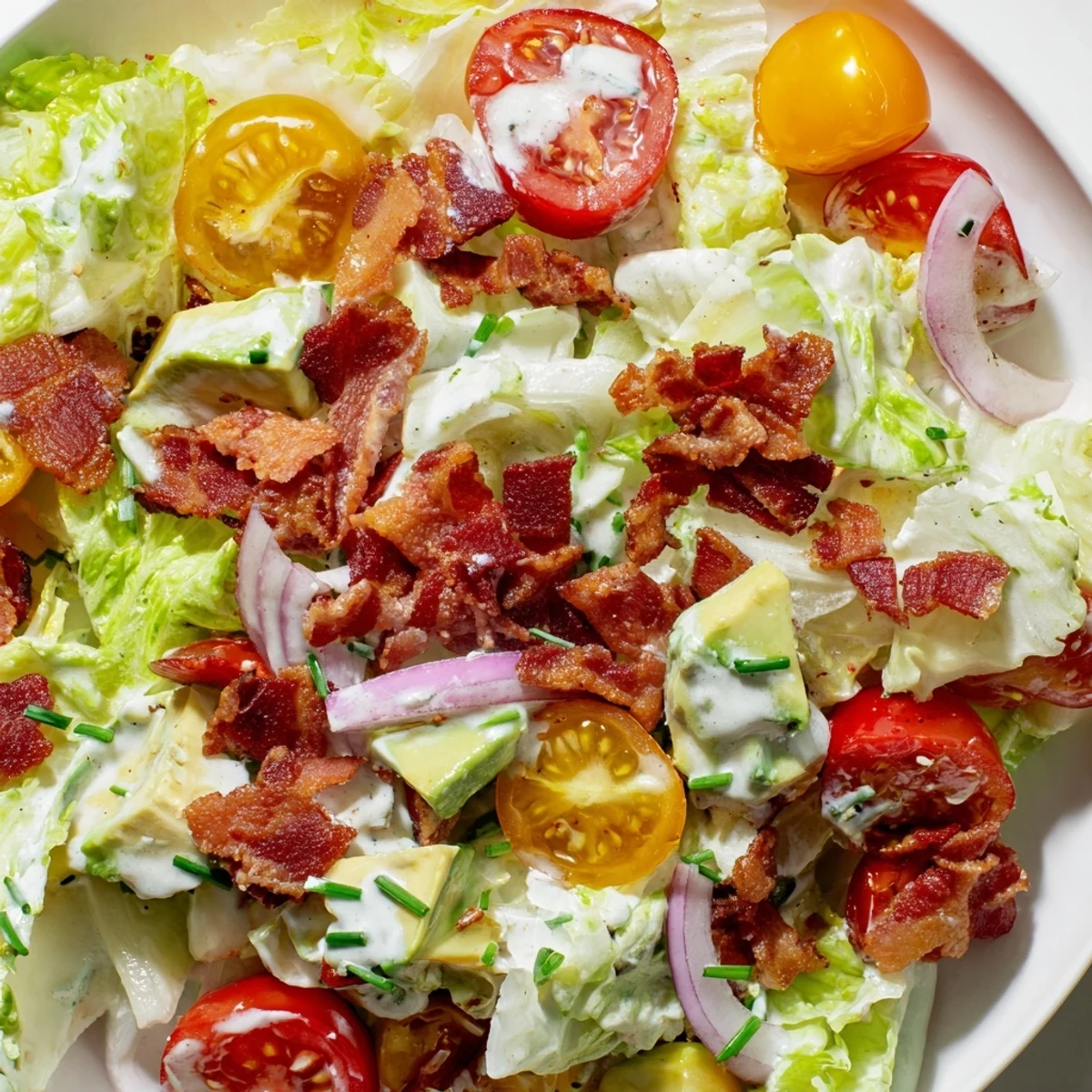 The Crispy Bacon Keto BLT Salad sits in a white bowl with cherry tomatoes and creamy dressing.
