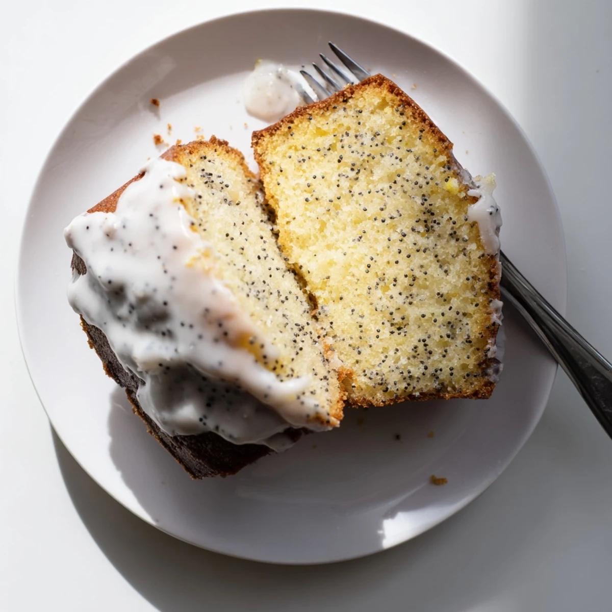 A glossy Lemon Poppy Seed Cake slice shows moist crumb and lemon glaze dripping over the top, ready for dessert.