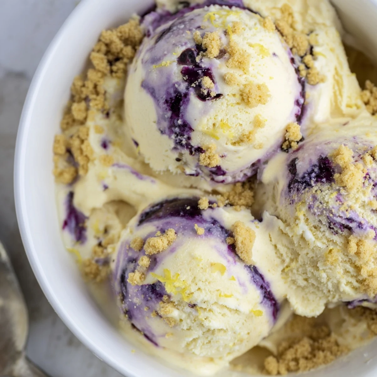 A close-up of homemade Lemon Blueberry Cheesecake Ice Cream in a white bowl with graham cracker crumbs.