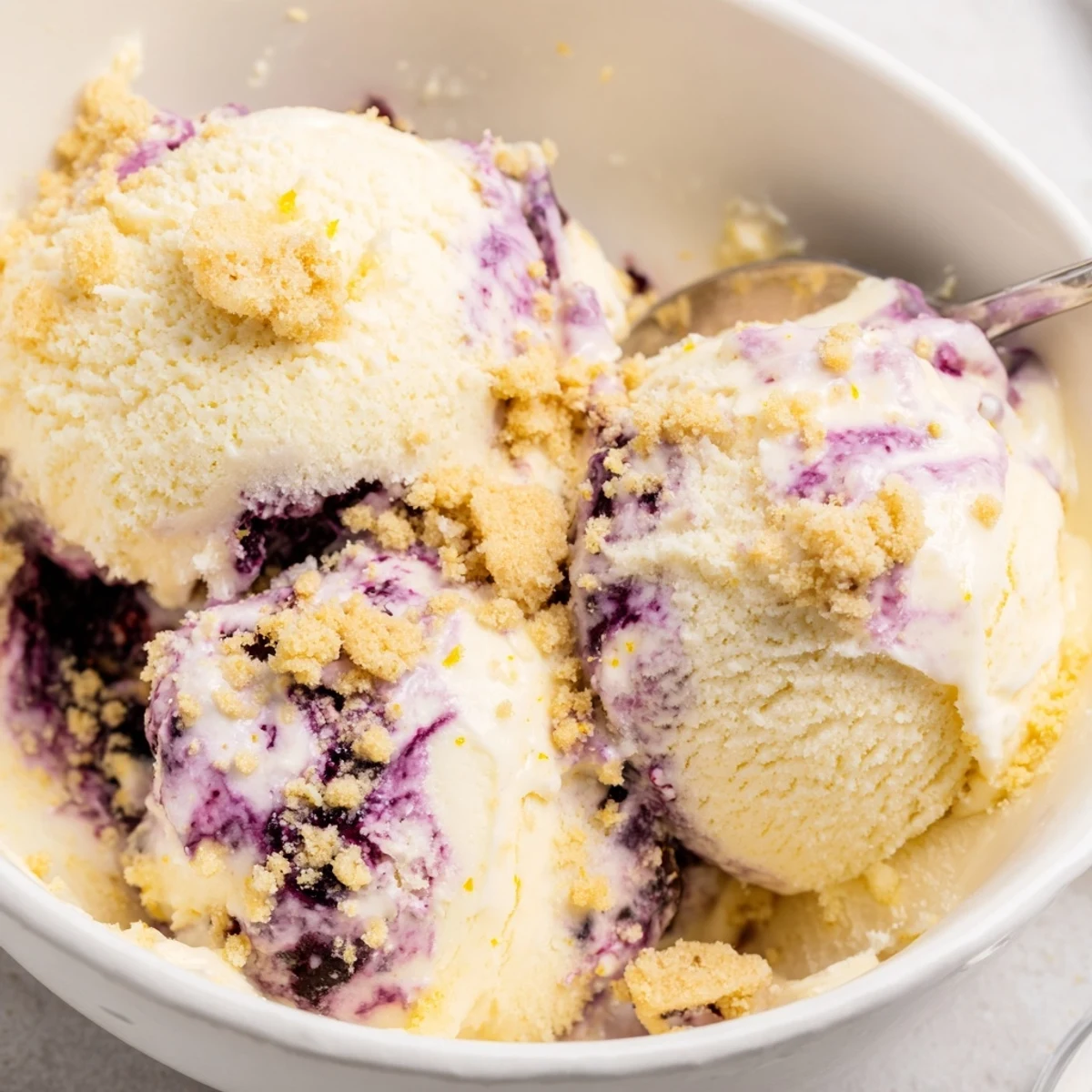 This scoops of creamy Lemon Blueberry Cheesecake Ice Cream shows the purple berry swirl and lemon zest.