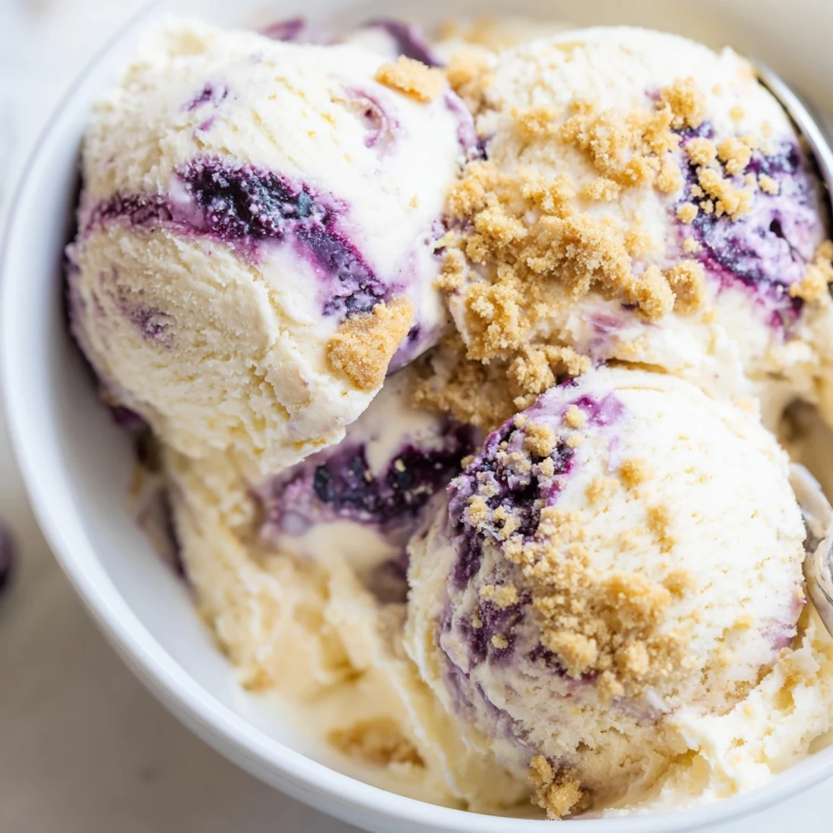 A frozen dessert bowl of Lemon Blueberry Cheesecake Ice Cream topped with a graham cracker crumble.