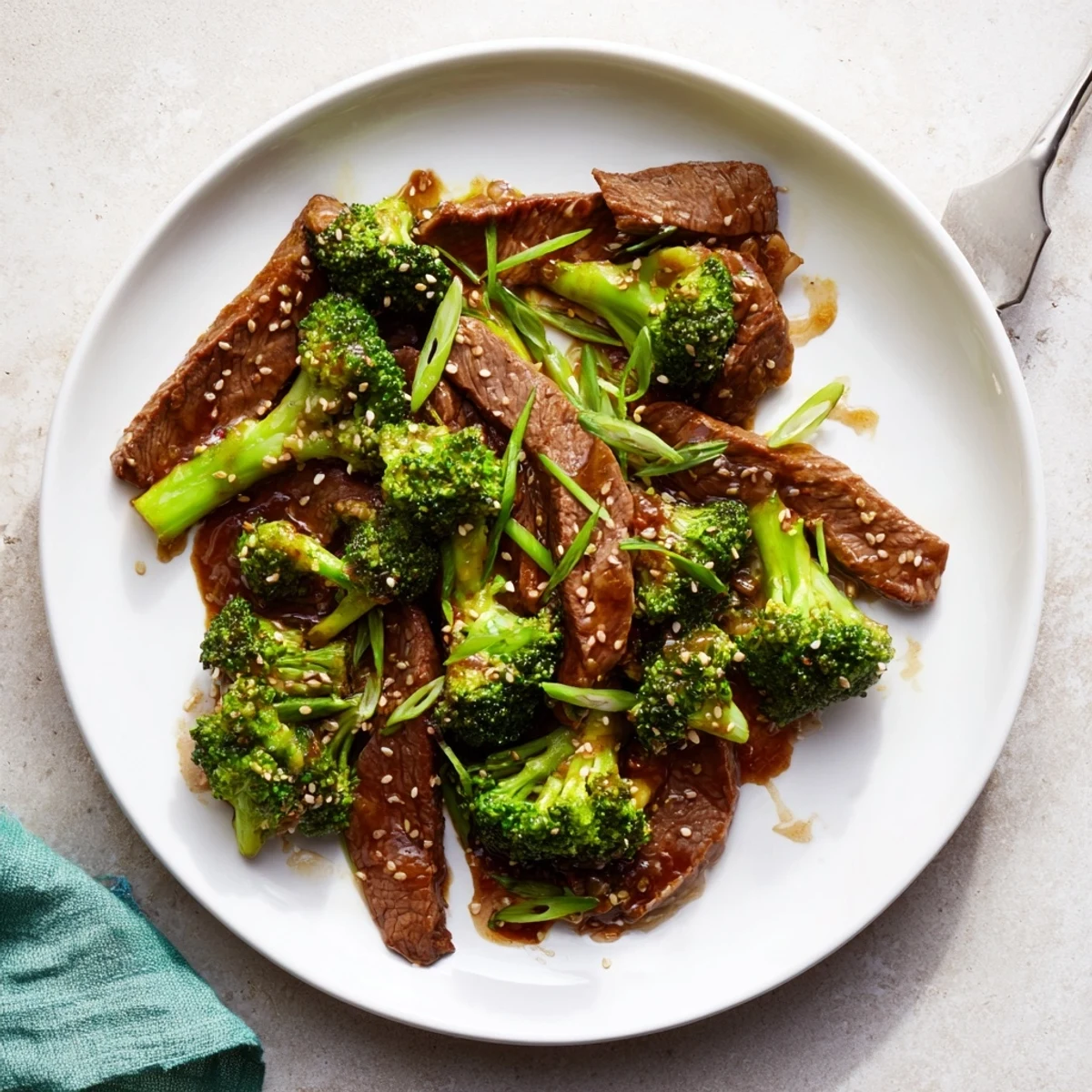 Tender beef slices and bright green broccoli coated in savory brown sauce for Better Than Takeout Beef With Broccoli on a white plate.