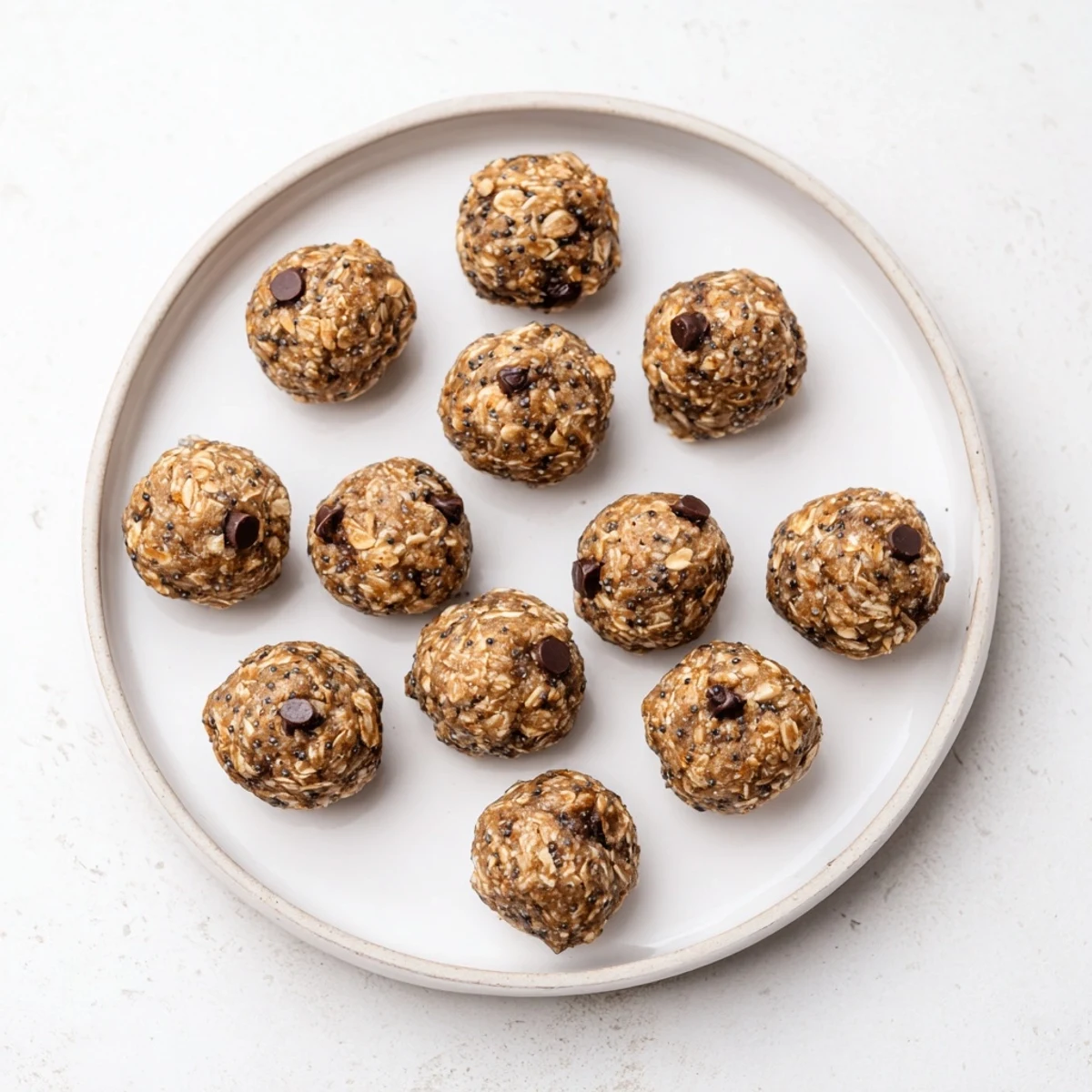 Close-up of mint chocolate chip protein balls showing melted mini chocolate chips and rolled oats on a clean marble background. 