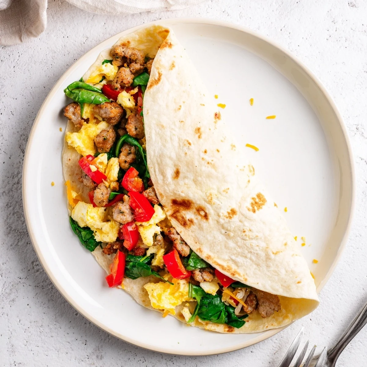 Sliced make-ahead breakfast burrito revealing eggs, cheese, and vegetables inside a soft flour tortilla