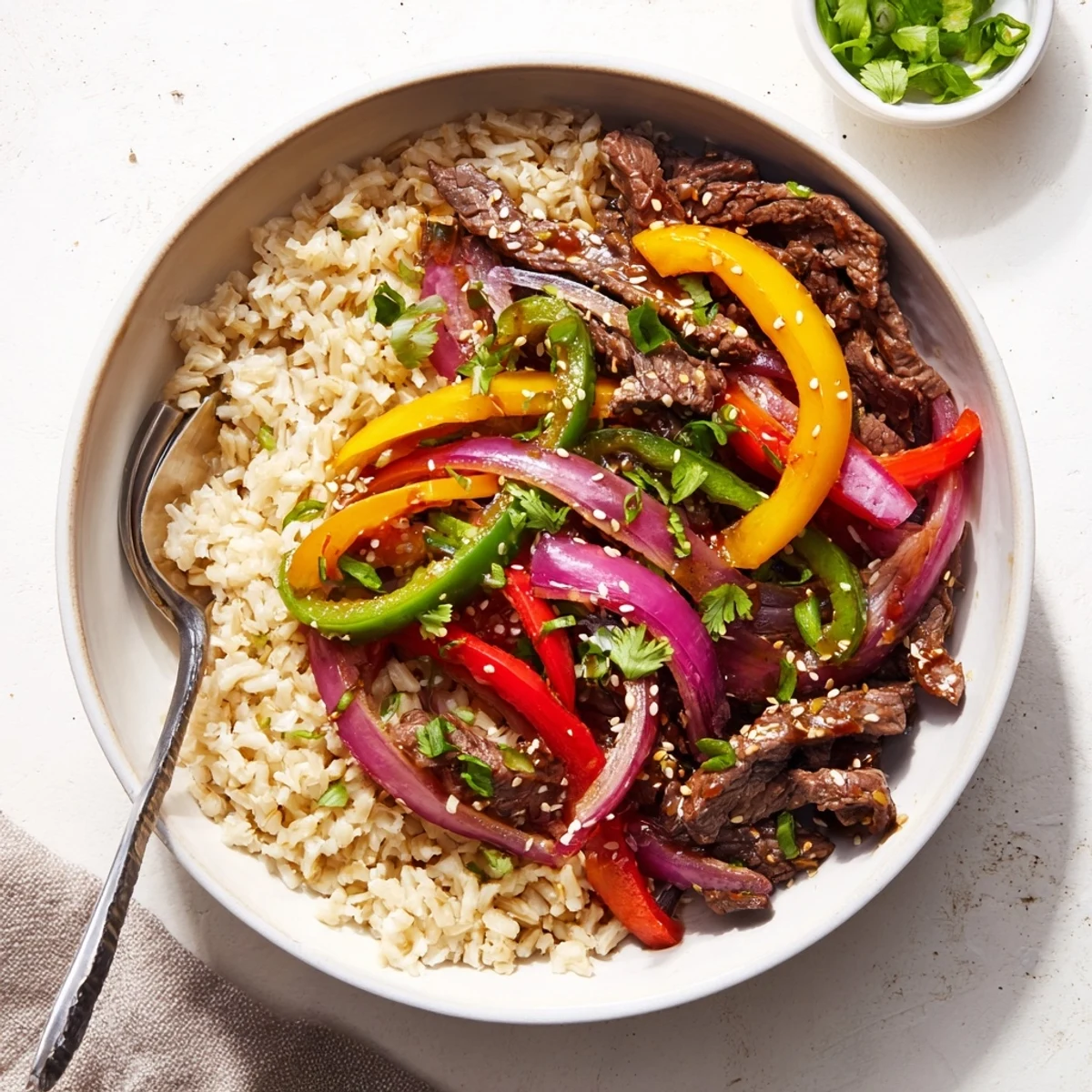 Savory Asian-inspired healthy beef and pepper rice bowl showcasing marinated beef strips and rainbow bell peppers served atop steamed brown rice with drizzled glaze