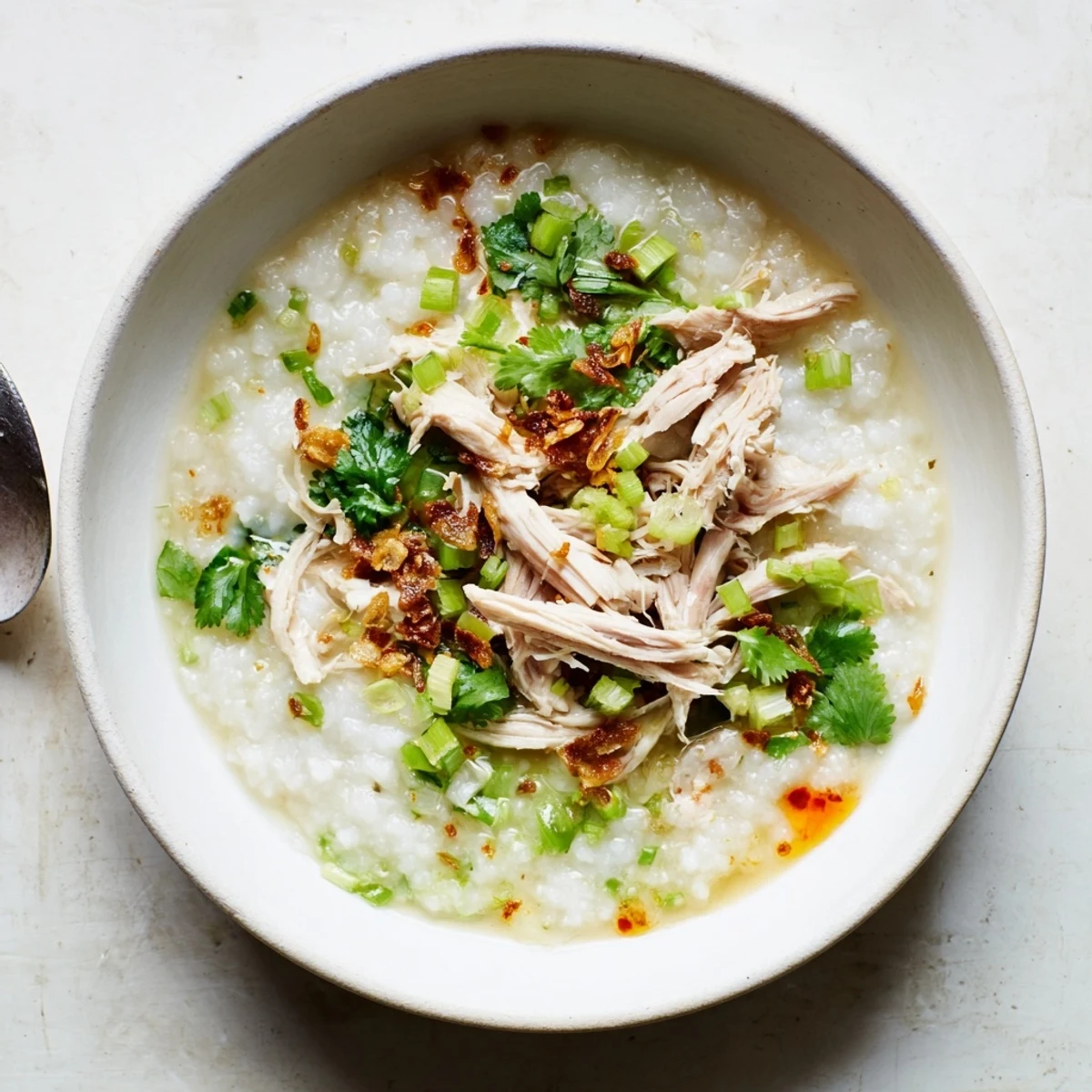 Creamy leftover Thanksgiving turkey congee topped with scallions, cilantro, and crispy shallots in a white bowl