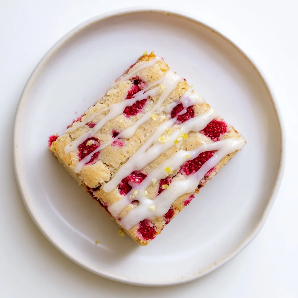 Golden Raspberry Lemon Blondies drizzled with zesty glaze on a white serving plate