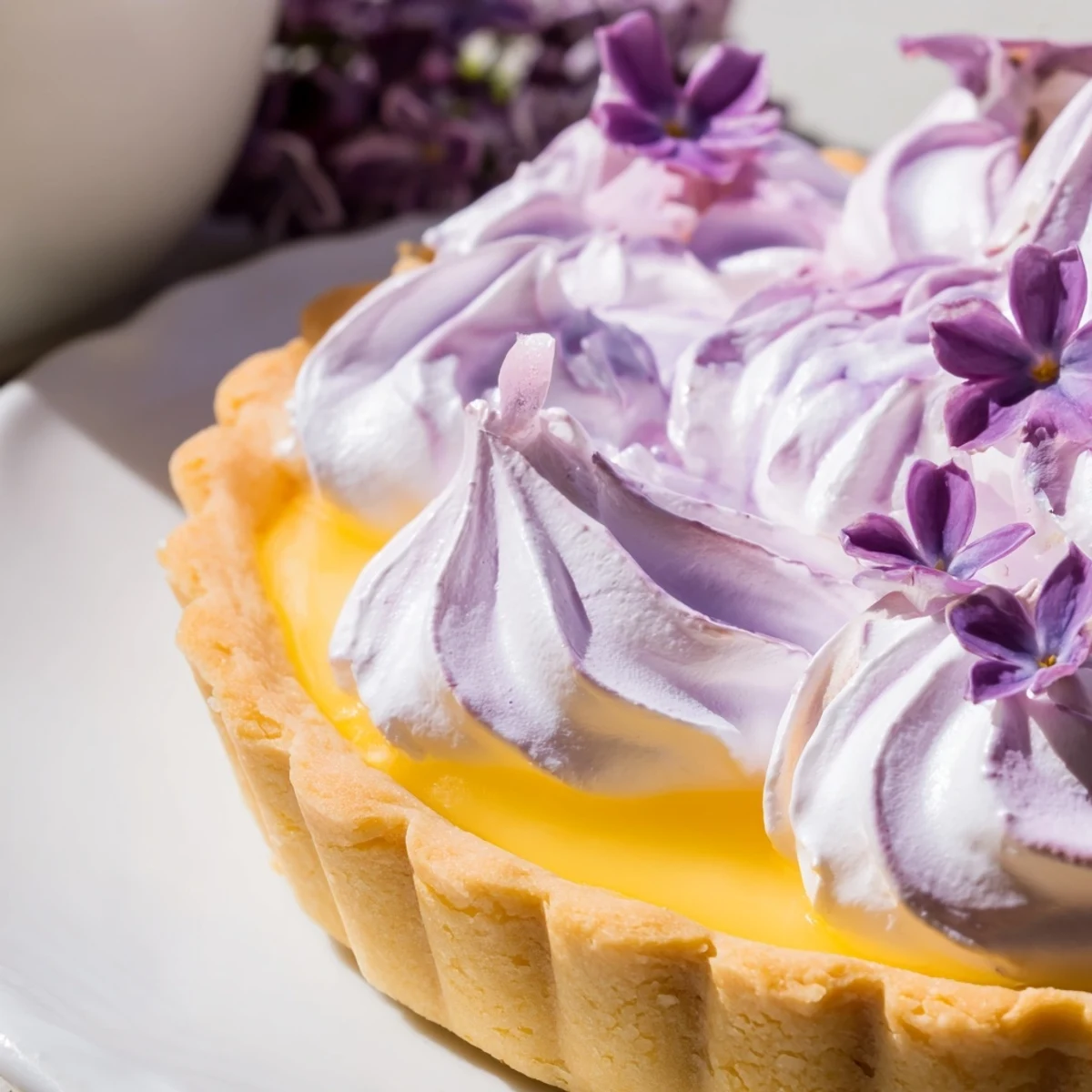 Floral lilac meringue mini lemon tart with bright yellow curd in a crisp buttery shell