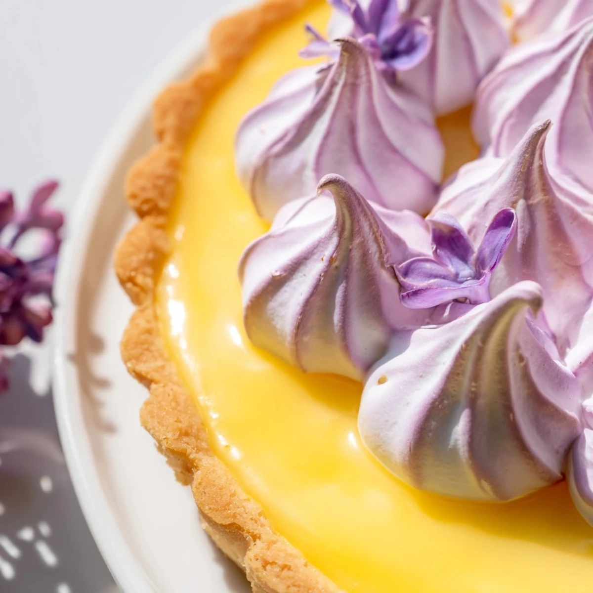 Handheld mini lemon tart featuring fluffy lilac meringue garnished with delicate purple flowers