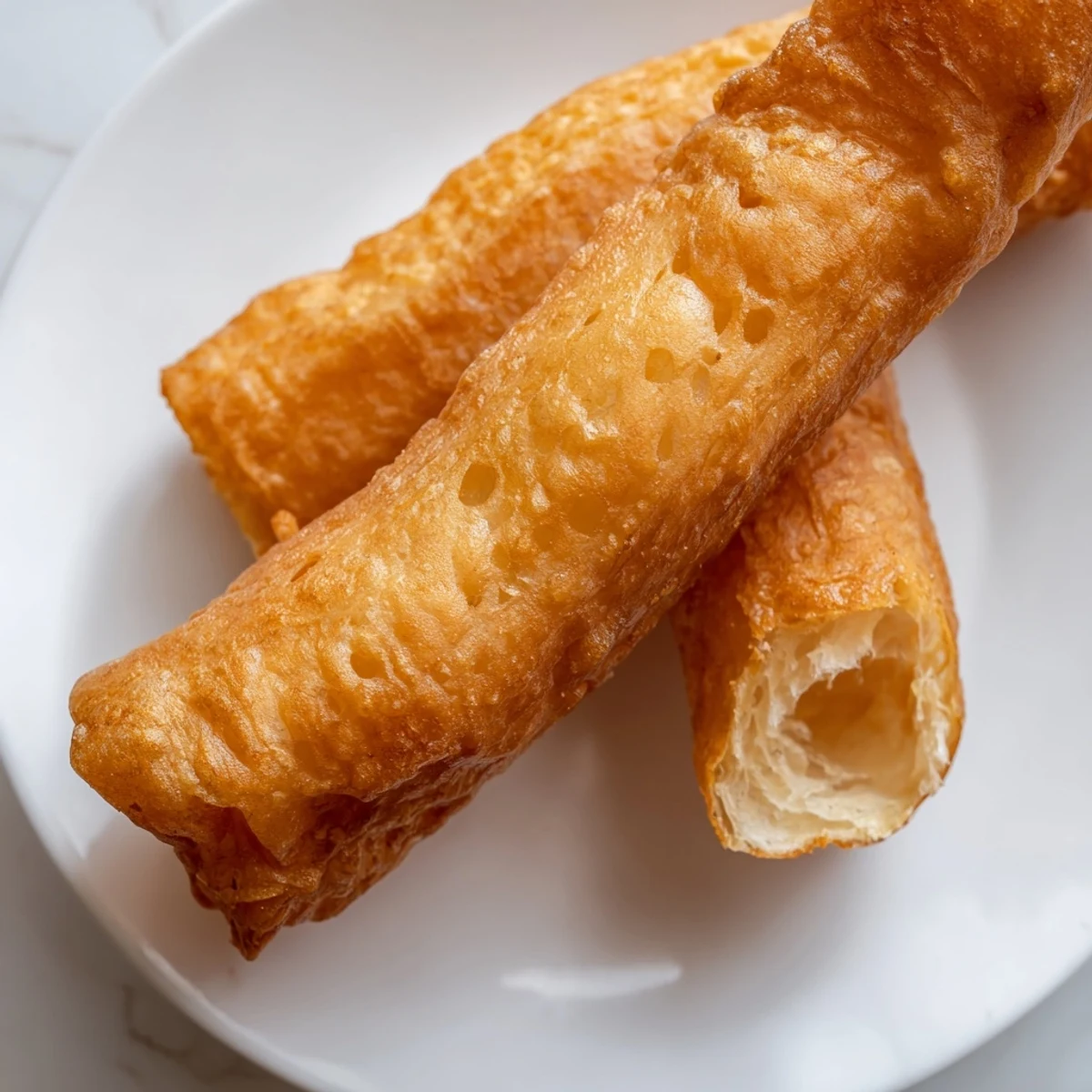 Golden fried Youtiao Chinese doughnuts rest on a wire rack after deep frying