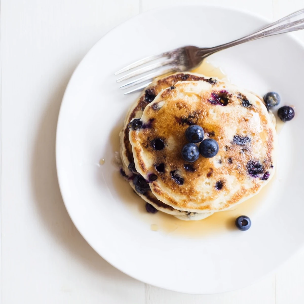 Golden stack of fluffy Greek yogurt blueberry pancakes drizzled with maple syrup