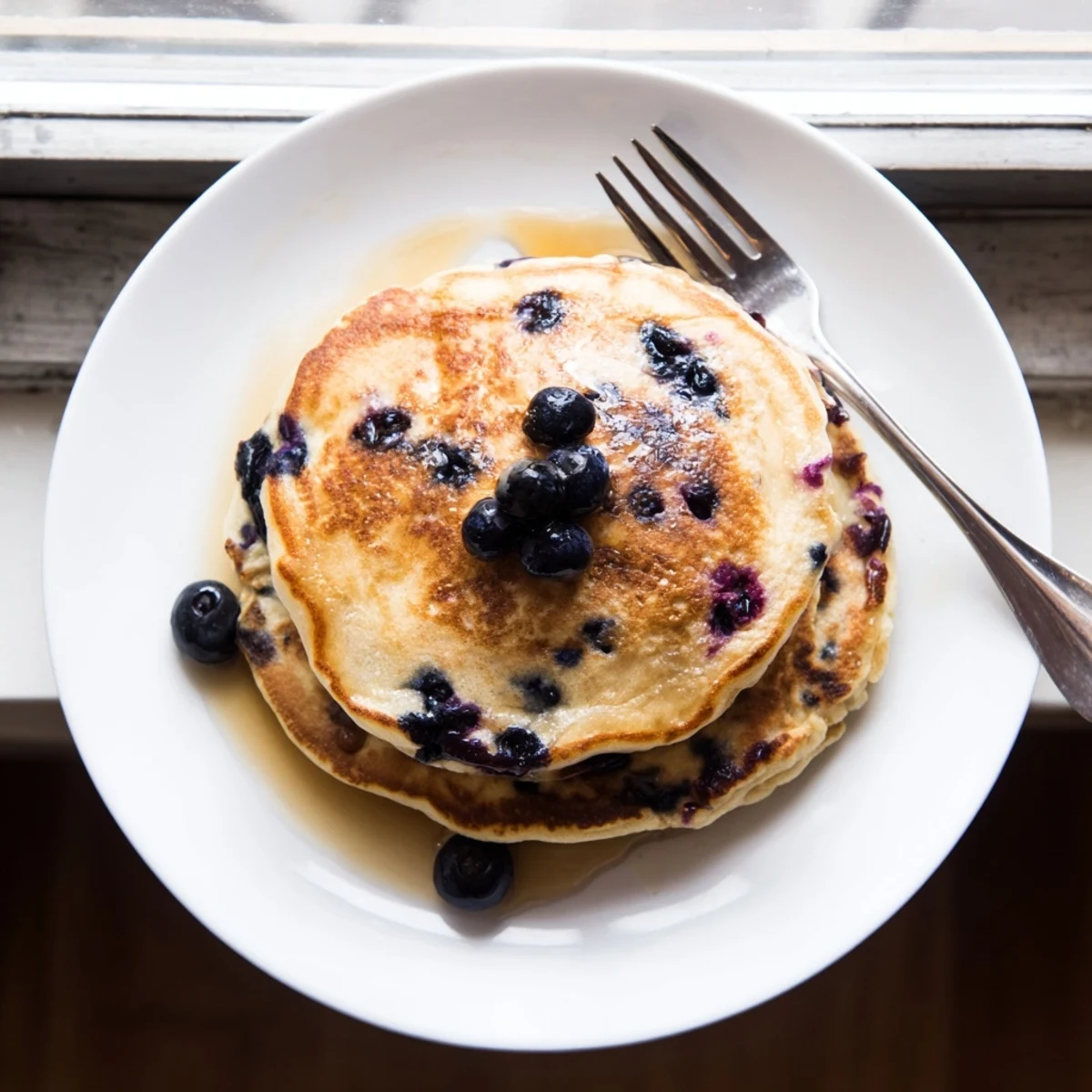 Fluffy Greek yogurt blueberry pancakes on a white plate with fresh blueberry garnish