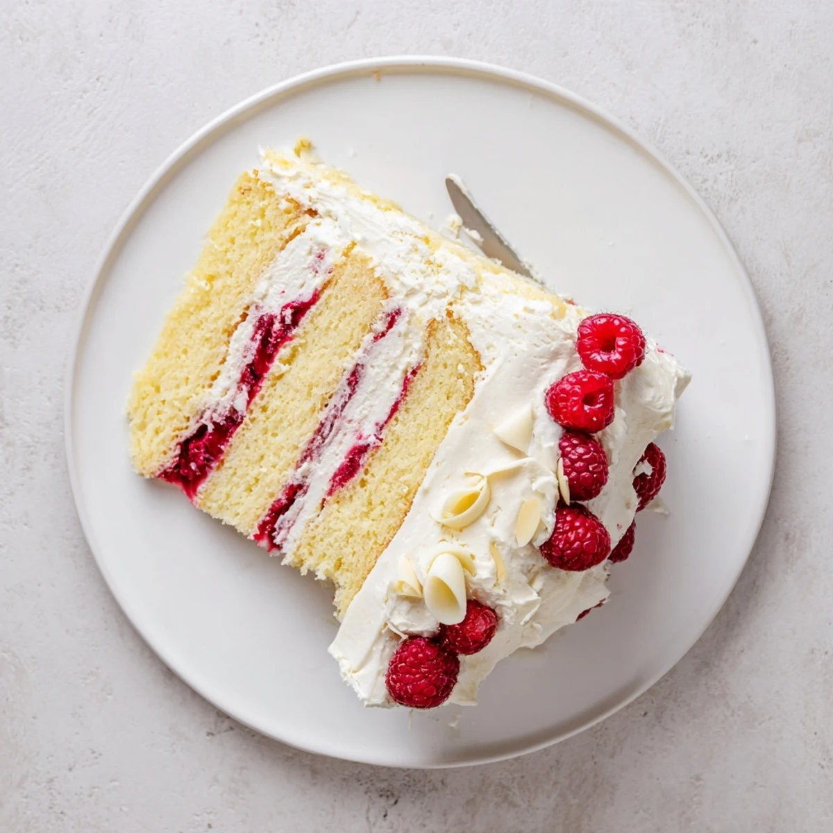 Sliced white chocolate raspberry cream cake revealing layers of fluffy vanilla sponge and tart raspberry compote