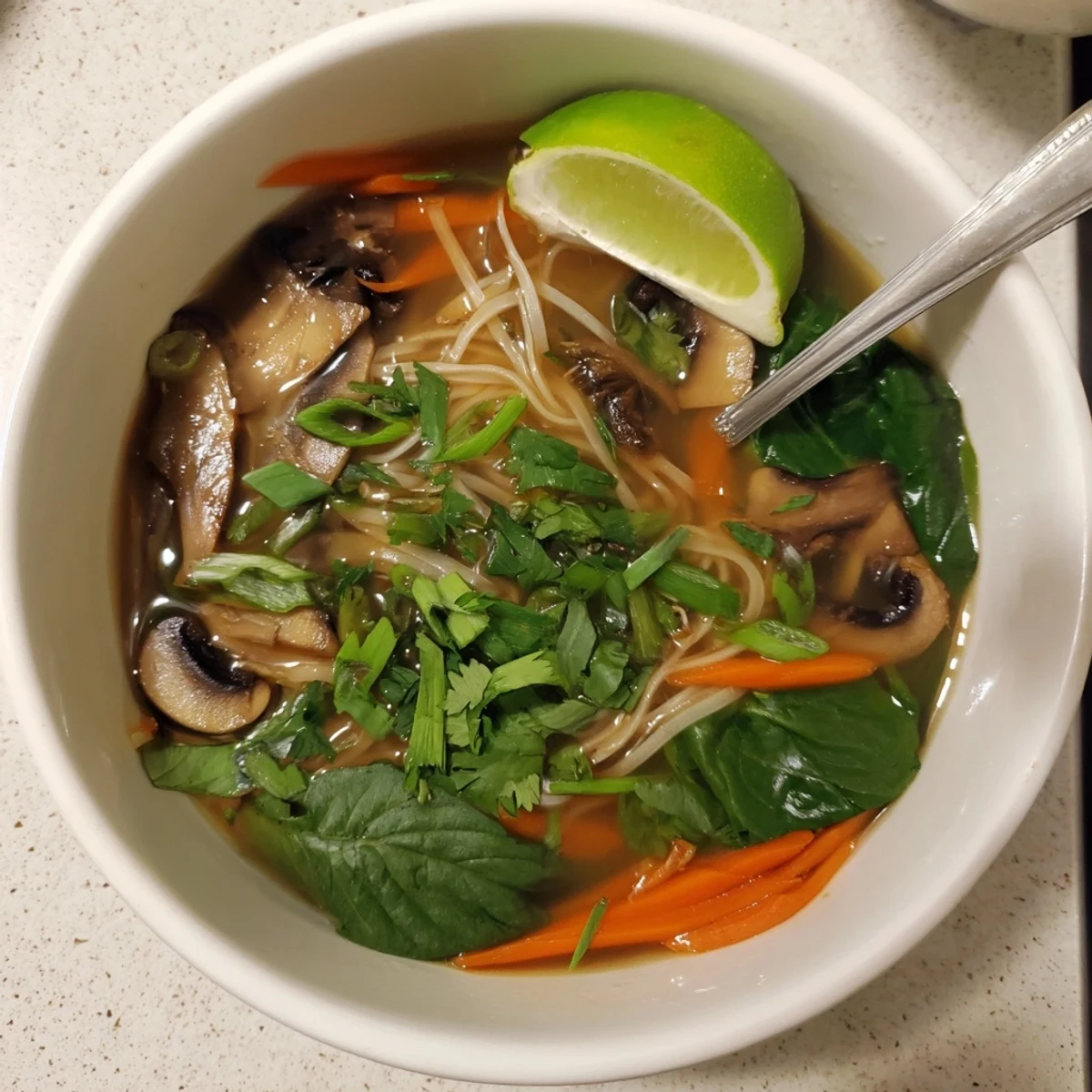 Steaming bowl of healing ginger garlic broth with rice noodles garnished with fresh cilantro and lime
