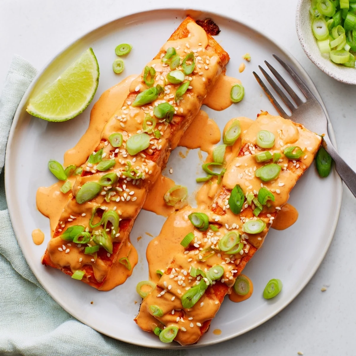 Tender flaky Bang Bang Salmon resting on a white plate drizzled with thick sweet chili mayonnaise sauce