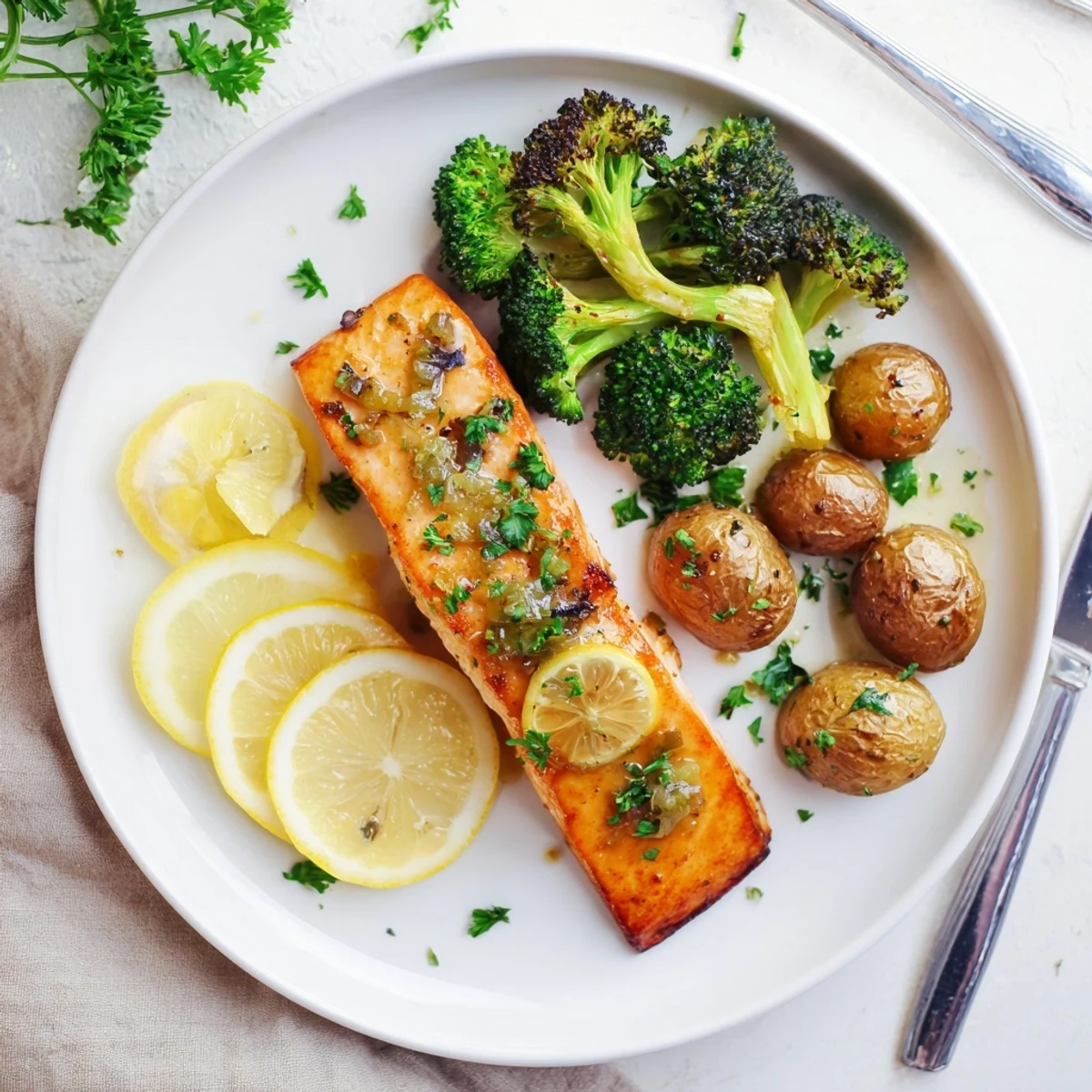 Golden pan-seared salmon fillets drizzled with zesty lemon butter sauce alongside crispy roasted potatoes and tender green broccoli florets on a white serving plate