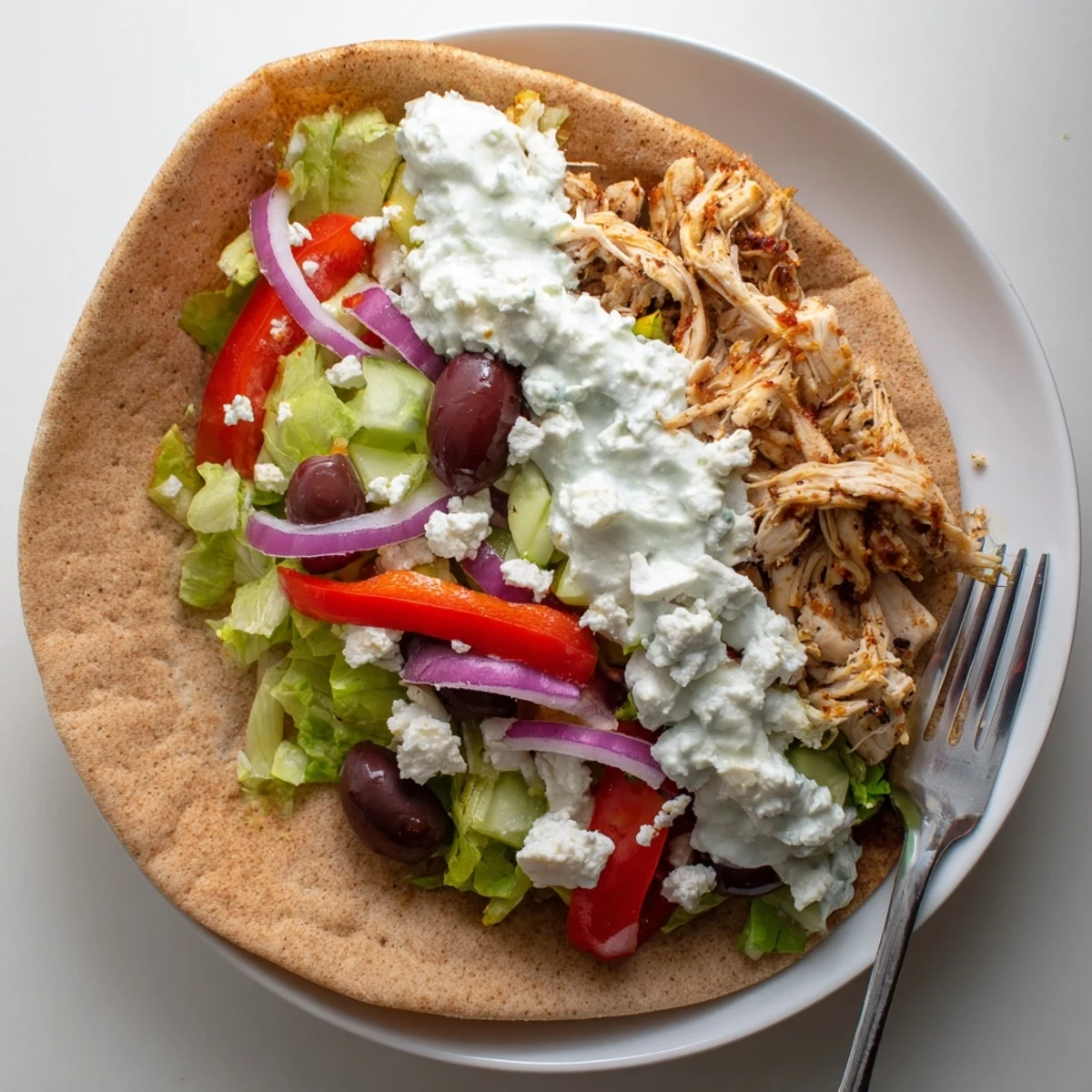Homemade Greek chicken pitas featuring slow-cooked seasoned meat with fresh lettuce tomatoes and tangy yogurt sauce