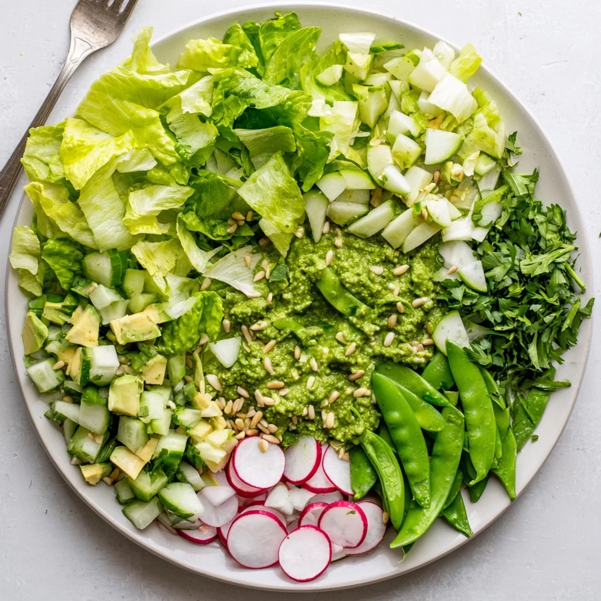 Vibrant green goddess salad featuring mixed greens, snap peas, radishes, and tangy homemade dressing layered in a white bowl