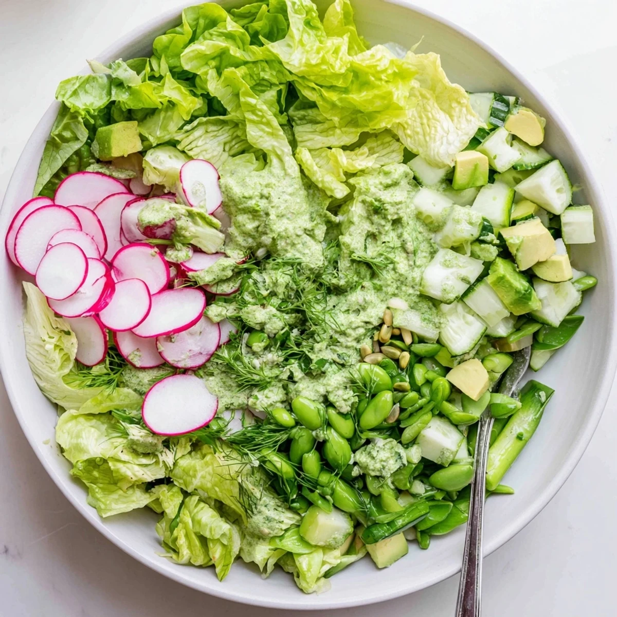 Colorful green goddess salad topped with diced avocado, fresh herbs, and sunflower seeds drizzled with vibrant green sauce