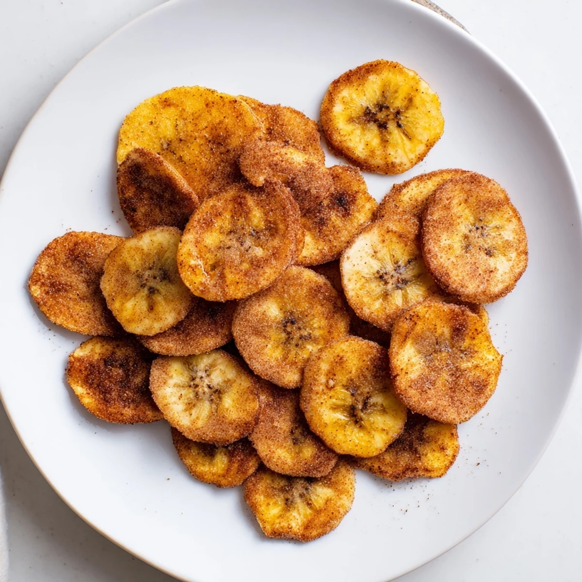 Golden cinnamon sugar air fryer banana chips arranged on a white plate with visible spice coating