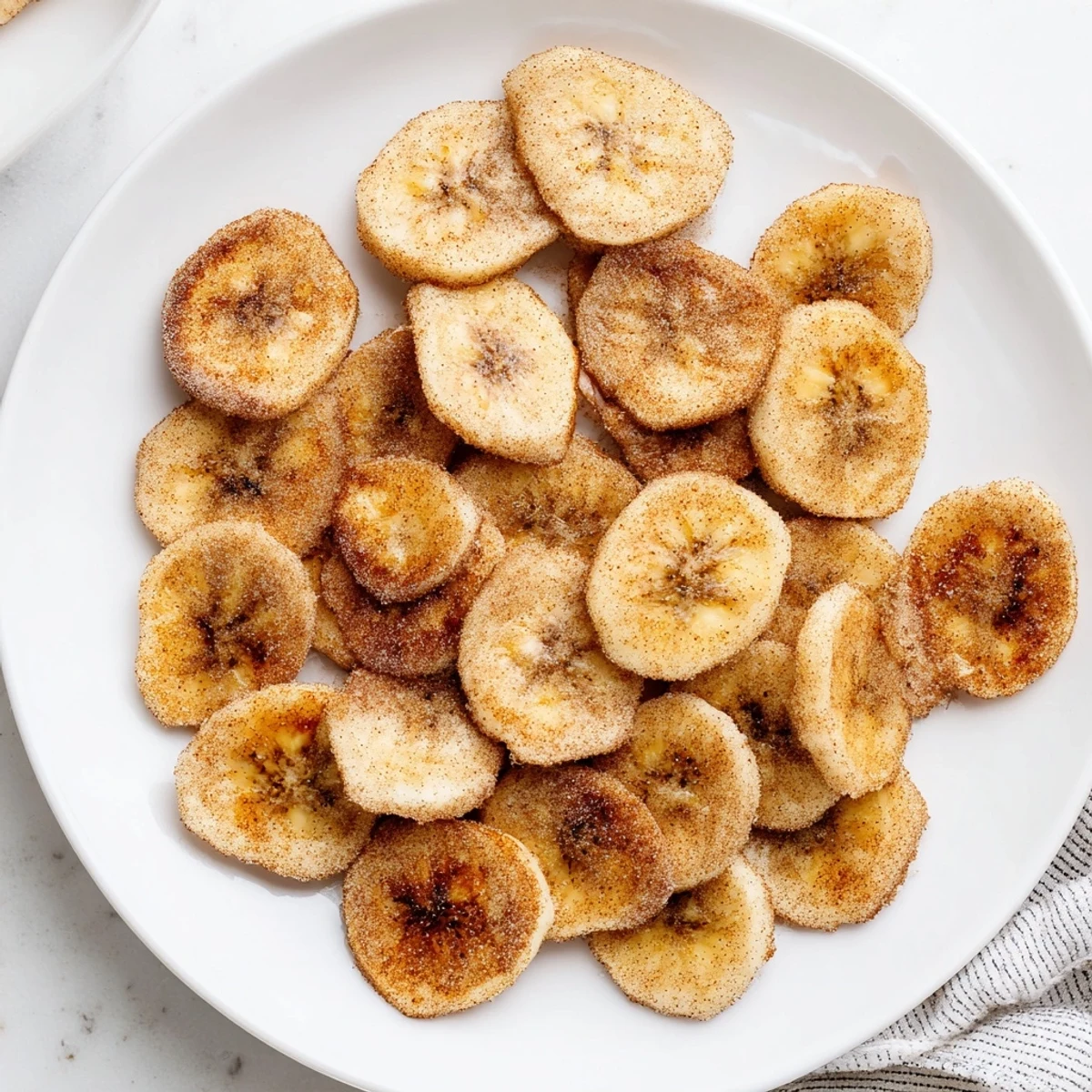 Crispy banana chips sprinkled with brown cinnamon sugar cooling on a wire rack after air frying