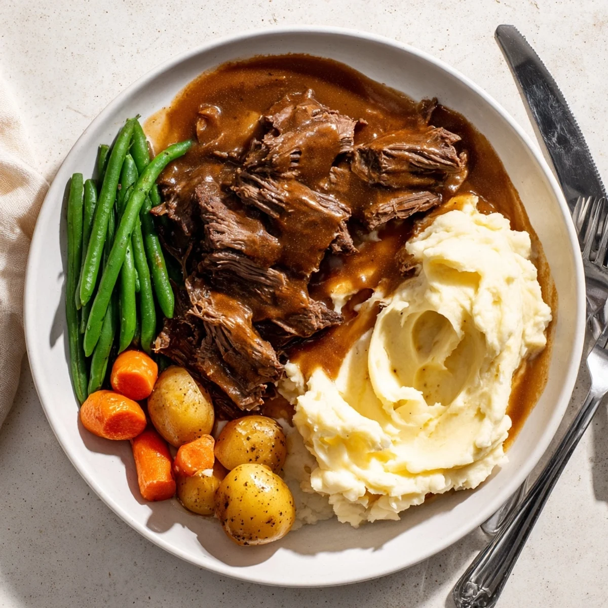 Golden brown Southern style pot roast plated with fluffy mashed potatoes and rich dark gravy drizzled over tender beef