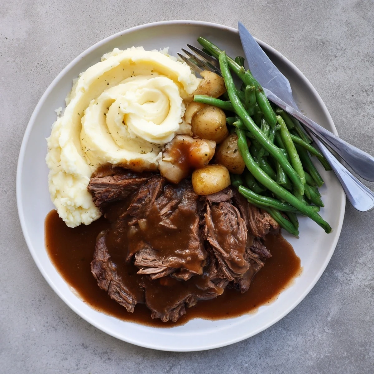 Fork-tender Southern style pot roast sliced and arranged beside buttery mashed potatoes and seasoned green beans on a rustic serving platter