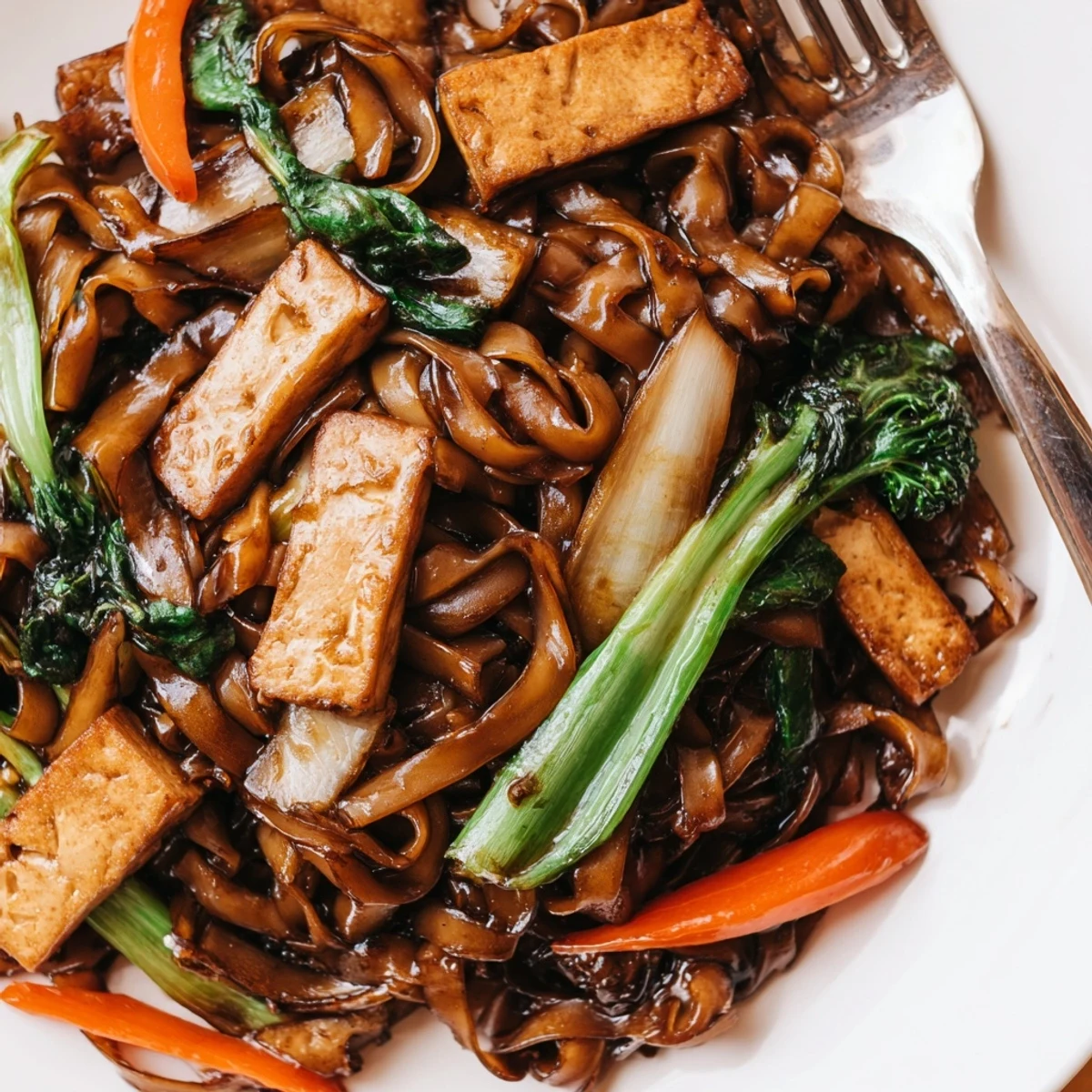 Vegan Pad See Ew stir-fried with wide rice noodles, crisp vegetables, and savory soy-based sauce in a dark glossy wok