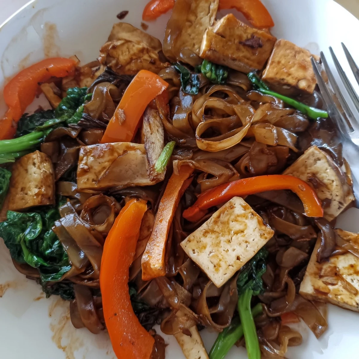 Close-up of Vegan Pad See Ew featuring charred rice noodles, tofu strips, Chinese broccoli, and fresh green onion garnish