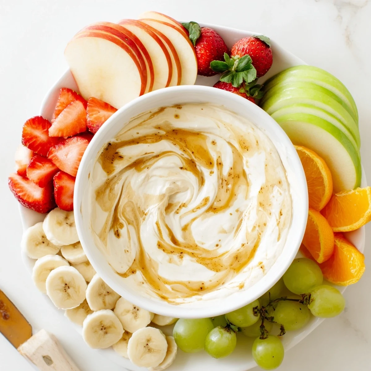 Creamy Greek yogurt cinnamon roll dip swirled with cinnamon and served with fresh sliced apples, strawberries, and grapes for a healthy snack
