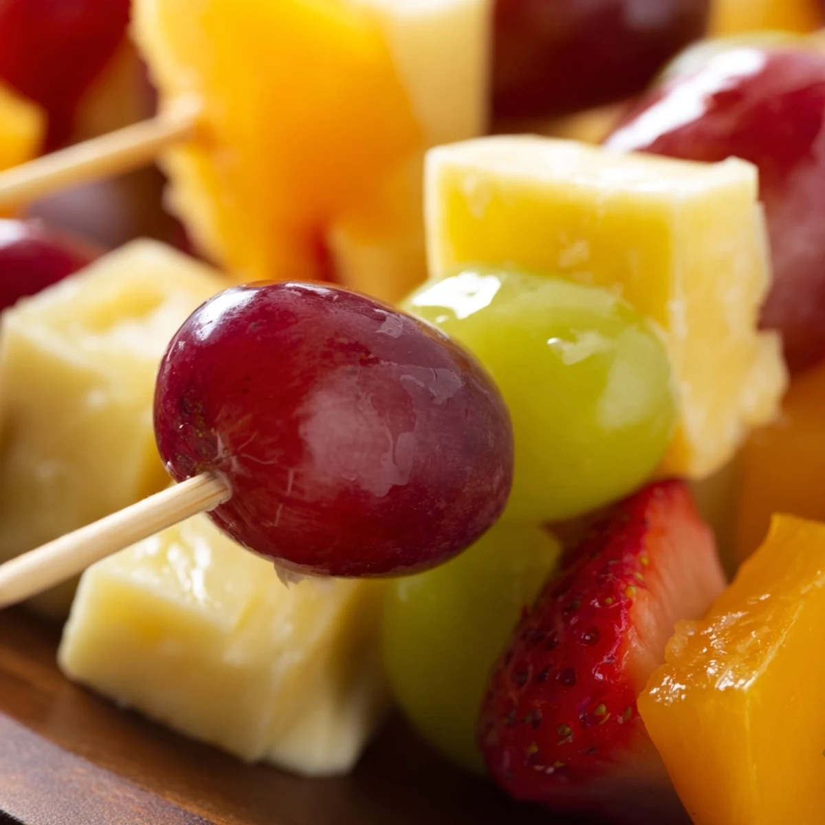 Colorful fruit and cheese kabobs arranged on a platter with grapes strawberries pineapple and cubed cheddar