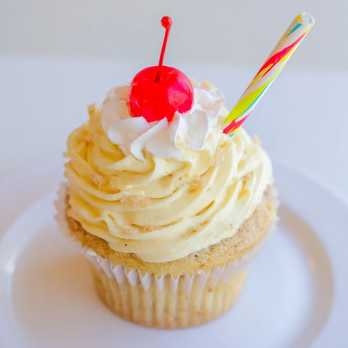 Golden banana milkshake cupcakes with fluffy whipped frosting served on a rustic white plate