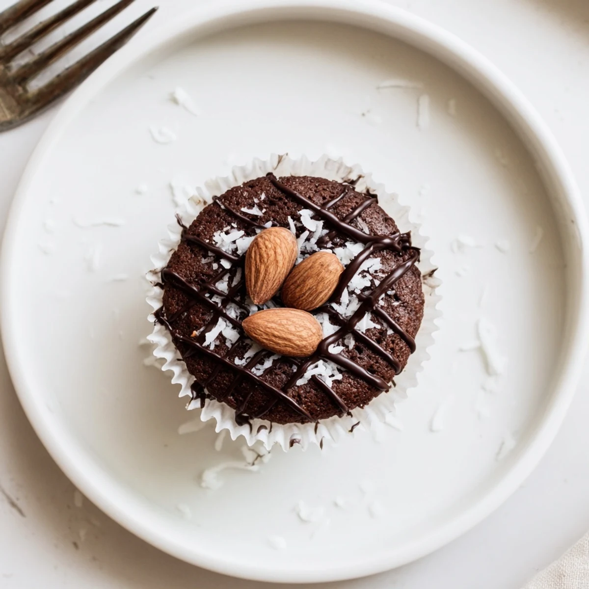 Flourless Almond Joy Cupcakes topped with chocolate drizzle and roasted almonds on a rustic plate