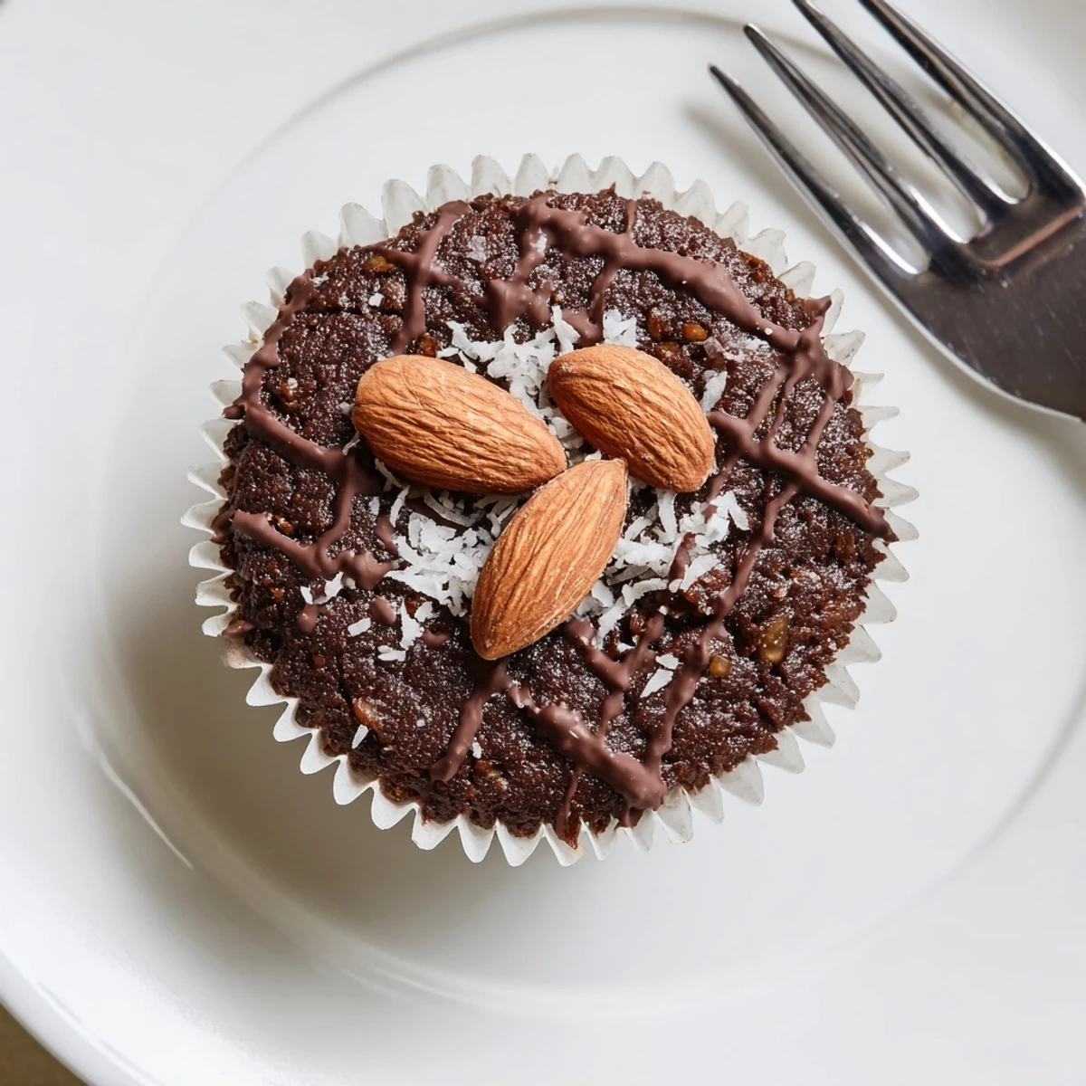 Decadent Flourless Almond Joy Cupcakes nestled in paper liners drizzled with melted chocolate and coconut flakes