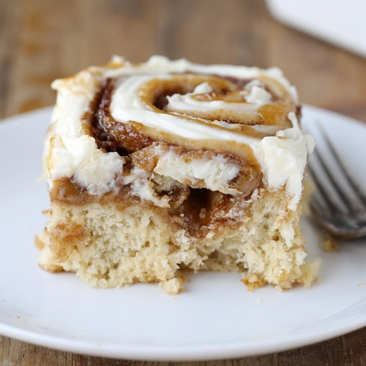 Sliced Cinnamon Roll Poke Cake served warm with melting cream cheese icing.