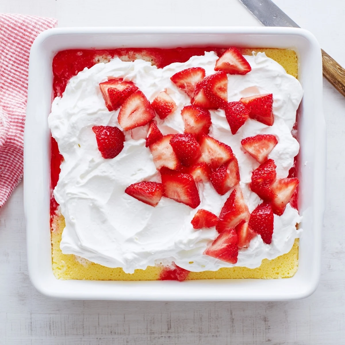 Strawberry gelatin cake with layers of fluffy yellow cake topped with whipped cream and fresh red strawberry slices