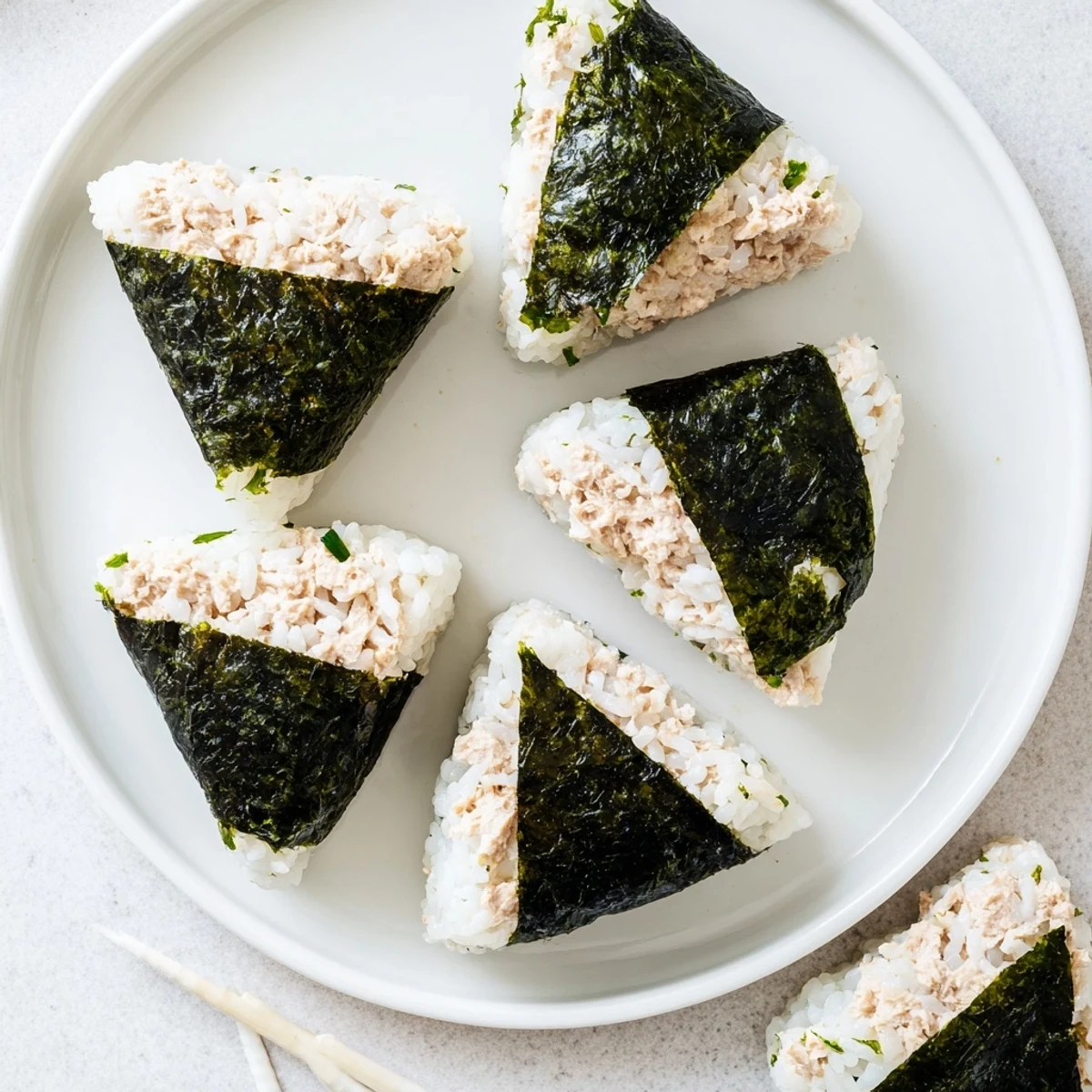 Golden triangular tuna mayo onigiri wrapped in crisp nori strips on white plate