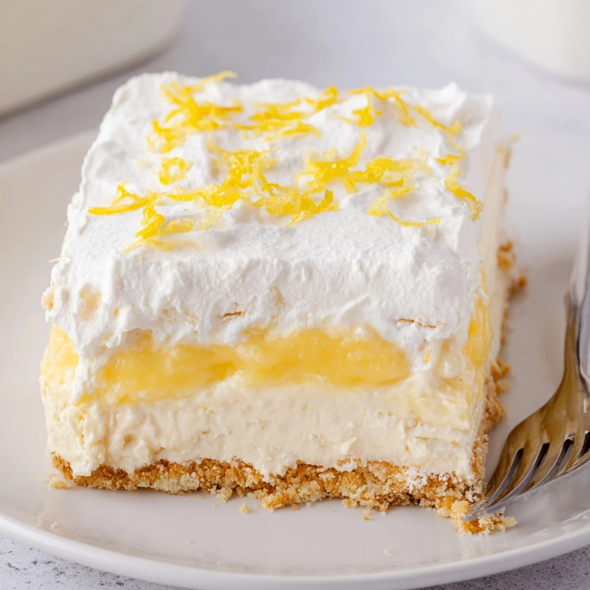 A slice of Lemon Lush Cake on a plate, creamy layers and crumbly crust