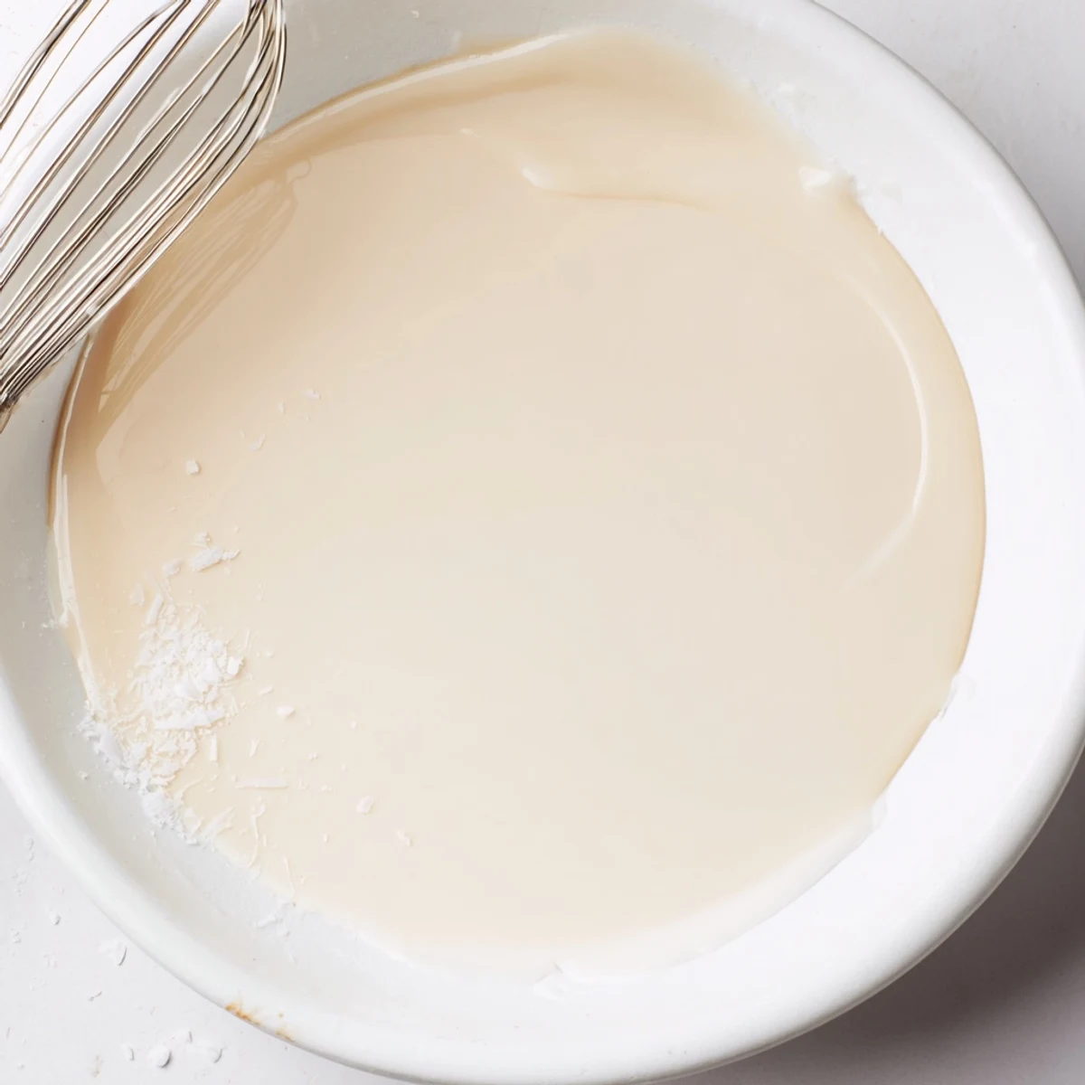 Thick golden condensed coconut milk drizzling from a spoon into a glass jar