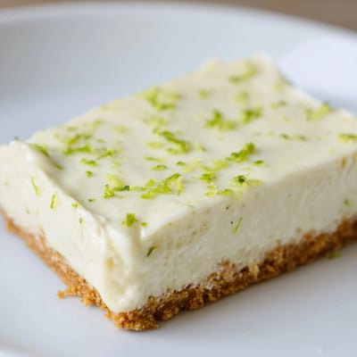 Golden Lime Bars with Graham Cracker Crust are dusted with powdered sugar and topped with lime zest and whipped cream.
